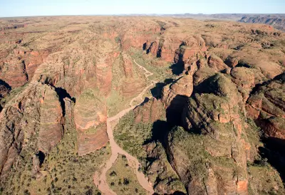 Aerial view of winding dry creek beds cutting between towering sandstone formations across the rugged Bungle Bungle landscape.
