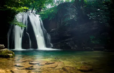 Long-exposure view of Janet's Foss waterfall flowing into a clear green pool surrounded by shaded woodland near Malham, North Yorkshire.