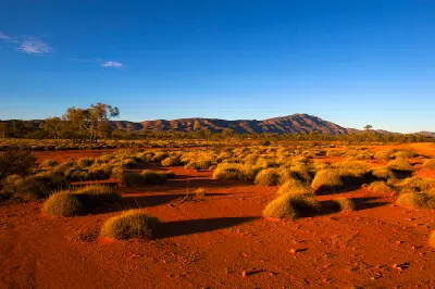 Red earth and spinifex grassland stretch towards the ridges of the West MacDonnell Ranges.