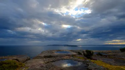 Shallow rock pools reflect breaks in dramatic storm clouds on the clifftop at Point Perpendicular, overlooking the ocean and Jervis Bay.