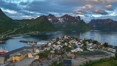 Drone view of Husøy island with clustered houses, harbour buildings, and Øyfjorden framed by mountainous terrain