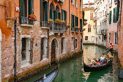 Gondola sailing through the canals of Venice, with tourists onboard moving between historic buildings.
