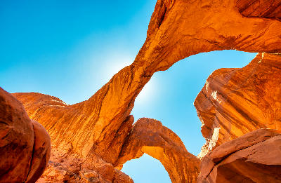 Looking up at Double Arch, showing two connected sandstone arches and blue sky in Arches National Park, Utah.