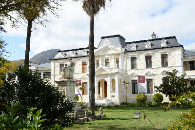 Historic Stellenbosch University building with palm trees and mountain backdrop in Stellenbosch, South Africa.
