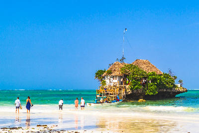 Visitors walking across the shallow lagoon towards The Rock Restaurant off Paje Beach, Zanzibar, Tanzania.