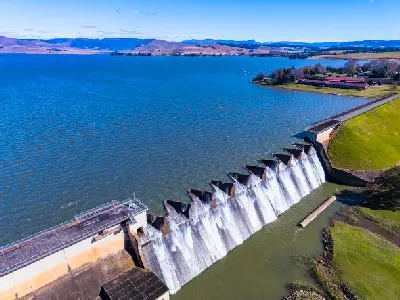 Aerial view of Midmar Dam and spillway near Howick, showing water flowing over the dam wall with the reservoir and surrounding Midlands countryside.