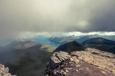 Cliff edge on Slættaratindur summit with fjords and mountain ridges below under heavy cloud, Eysturoy, Faroe Islands.