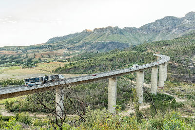 Elevated N1 highway bridge near Paarl, South Africa, curving across the Hugos River valley below the Drakenstein mountains with vehicles travelling through the Cape Winelands landscape.