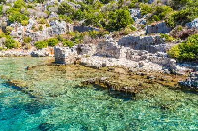 Ancient stone ruins extending into clear turquoise water along the coast of Kekova Island, Turkey.
