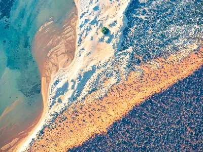 Aerial view of turquoise shallows, pale sand and red coastal scrub along the Francois Peron Peninsula.