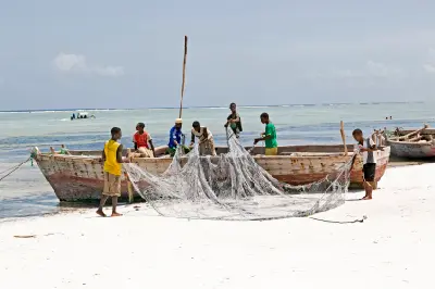 Local fishermen repairing fishing nets beside traditional wooden boats on Matemwe Beach, Zanzibar, Tanzania.