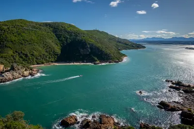 Aerial view of Featherbed Headland at Knysna Heads, showing rocky shoreline, forested slopes and turquoise waters at the entrance to Knysna Lagoon in South Africa.