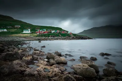 Rocks in the foreground with Elduvík village and white church on the coast of Eysturoy, Faroe Islands.