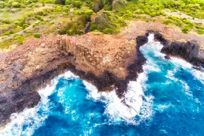 Aerial view of geometric basalt columns and rugged volcanic cliffs surrounded by turquoise ocean waves at Bombo Headland Quarry near Kiama.