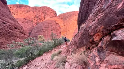 Walker on a rocky trail between towering red sandstone walls in Kings Canyon, Watarrka National Park, Australia.