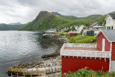 Mefjordvær fishing village on Senja island with red wooden house, coastal shoreline, and fjord backed by green mountains in northern Norway