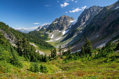 Cascade Pass view into alpine valley with forest, snow patches and rugged mountain walls in North Cascades National Park