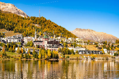 St. Moritz town and lake with autumn larch forest and mountain backdrop reflected in water, Engadin, Switzerland.
