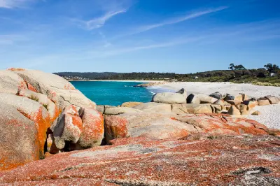Orange-lichen granite boulders beside a white sandy beach and turquoise sea at the Bay of Fires, Tasmania.