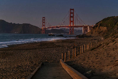 Golden Gate Bridge at dusk viewed from Baker Beach with a wooden boardwalk leading down to the shoreline