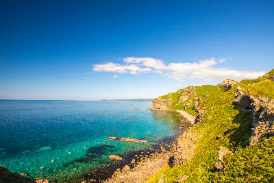 Green cliffs and rocky shoreline above clear turquoise water at Cape Kamui, Shakotan Peninsula, Hokkaido, Japan.