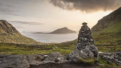 Cairn of stacked stones above Norðradalur valley with Koltur island in the North Atlantic at sunset, Streymoy, Faroe Islands.