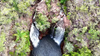 Overhead aerial view of two waterfalls flowing over reddish rock formations into a dark plunge pool surrounded by green tropical vegetation at Florence Falls, Litchfield National Park, Northern Territory, Australia.