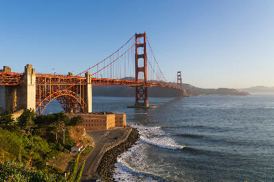 Golden Gate Bridge in warm morning light viewed from Fort Point with waves along the San Francisco shoreline