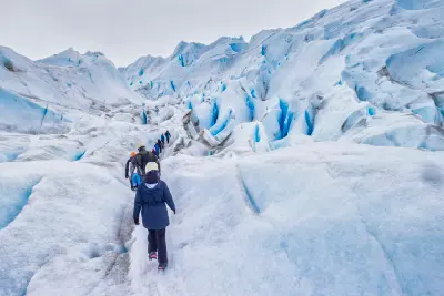 Tourists hiking on Perito Moreno Glacier with blue ice crevasses and rugged glacier surface in Patagonia, Argentina.