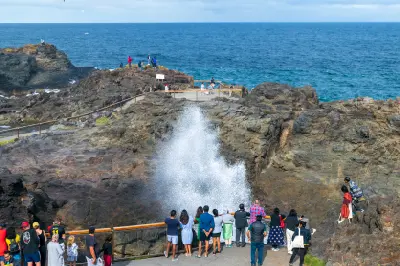 Visitors gather at the viewing platform as a large plume of seawater erupts from the Kiama Blowhole against the Pacific Ocean.