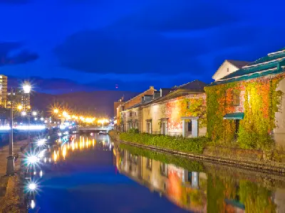 Evening light along Otaru Canal highlights the preserved warehouse facades, where warm street lamps reflect across still water and define the linear composition of the canal.