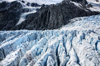 Crevassed ice formations of Franz Josef Glacier beneath steep alpine peaks in Westland Tai Poutini National Park, South Island, New Zealand.