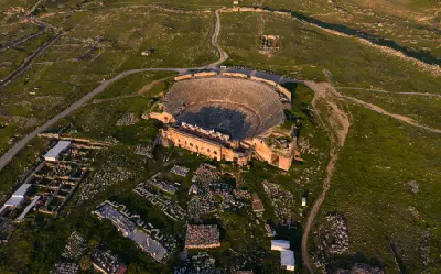 Aerial view of Hierapolis showing its large Roman theatre surrounded by ancient stone ruins and green landscape near Pamukkale.