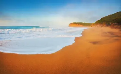 Waves and whitewater washing across the broad sandy shore beneath golden coastal cliffs at Bells Beach on Victoria’s Great Ocean Road.
