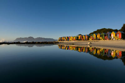 Colourful bathing huts at St James Beach reflected in a tidal pool at sunrise on the False Bay coast in Cape Town, South Africa.