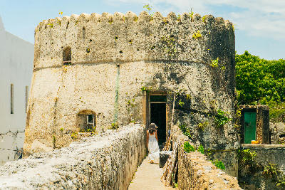 Woman walking along the coral stone ramparts of the Old Fort in Stone Town, Zanzibar, beside a historic watchtower.