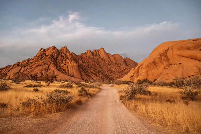 Desert road approaching the granite peaks and rock formations of Spitzkoppe in Namibia at sunset.