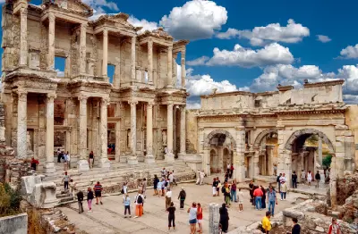Library of Celsus and adjoining ancient ruins at Ephesus, with visitors gathered around the monumental marble façade.