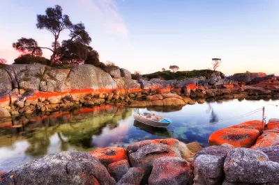 Small fishing boat moored in clear water among orange-lichen granite rocks at Binalong Bay, Tasmania.