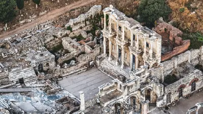 Elevated aerial view of the Library of Celsus in Ephesus, showing its ornate two-storey façade surrounded by excavated Roman streets, walls and buildings.