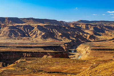 Sunlit desert landscape across Fish River Canyon in Namibia showing layered rock formations, canyon walls, and the winding river below under a clear blue sky.