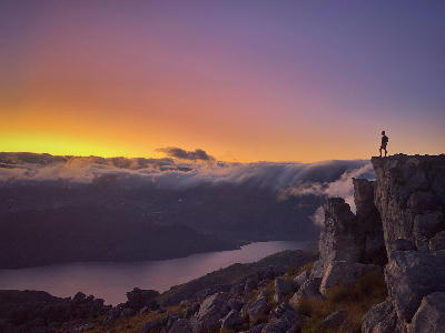 Trail runner on rocky summit overlooking mountain landscapes at dawn in Mont Rochelle Nature Reserve near Franschhoek, South Africa.