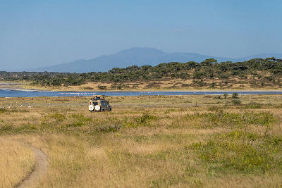 Safari vehicle driving across the Ndutu Plains beside Lake Ndutu with the Ngorongoro Highlands rising in the distance, Tanzania.