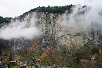 Staubbach Falls dropping down a cliff through mist above trees and houses in Lauterbrunnen Valley Switzerland