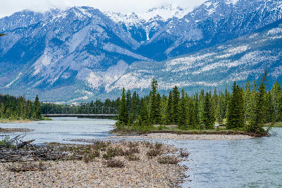 Athabasca River with forested banks and bridge beneath snow-capped mountains in Jasper National Park