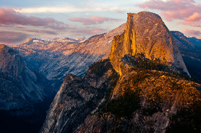 Half Dome at sunset from Glacier Point Yosemite with glowing granite face and layered mountain ridges under pink clouds.