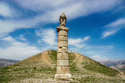 Ancient stone column topped by an eagle statue beside the Karakuş Tumulus in the mountainous landscape of Adıyaman, Turkey.