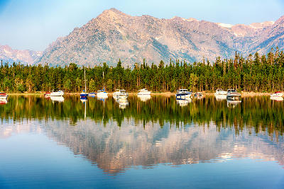 Marina boats on Jackson Lake with forest and Mount Moran reflected in still water in Grand Teton National Park, Wyoming, USA.