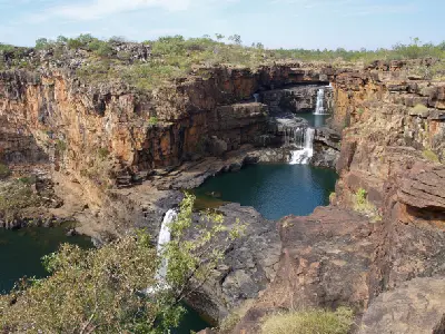 Wide view of Mitchell Falls cascading through multiple sandstone tiers into deep pools enclosed by rugged Kimberley cliffs.