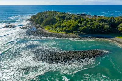 Aerial view of waves breaking around the rocky shoreline and dense coastal vegetation of Bombo Headland near Kiama.